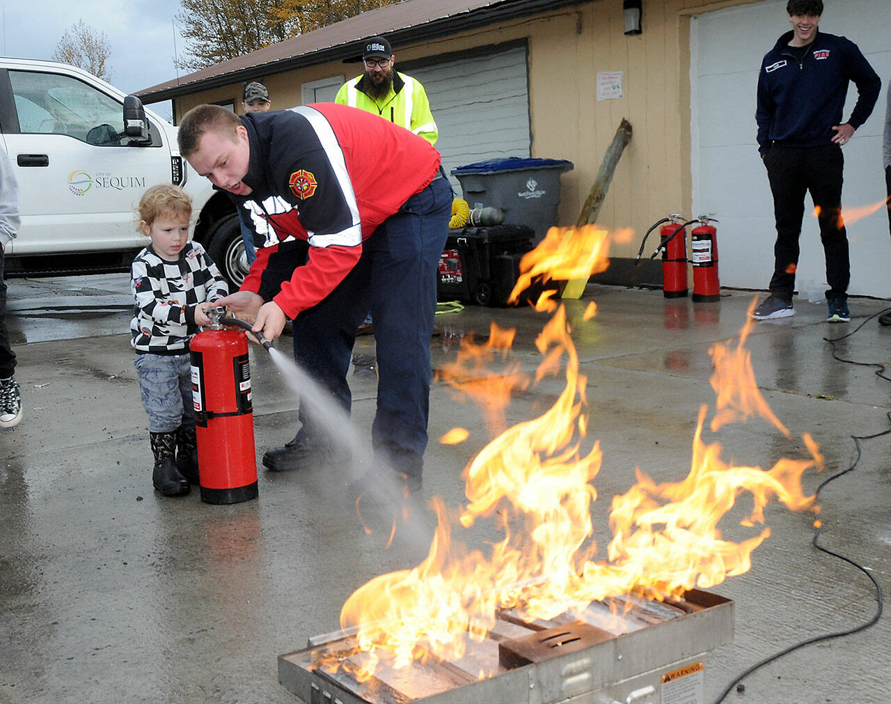 Beau Rossi, 2, of Sequim gets assistance from Clallam County Fire District 3 firefighter/paramedic Hayden Pyle with extinguishing an intentional propane fire during Saturday’s Public Safety and Information Fair at Carrie Blake Park in Sequim. The event, organized by Fire District 3 and the Community Emergency Response Team, featured a variety of exhibits and displays from numerous public safety and community service agencies, as well as workshops and children’s activities. (Keith Thorpe/Peninsula Daily News)