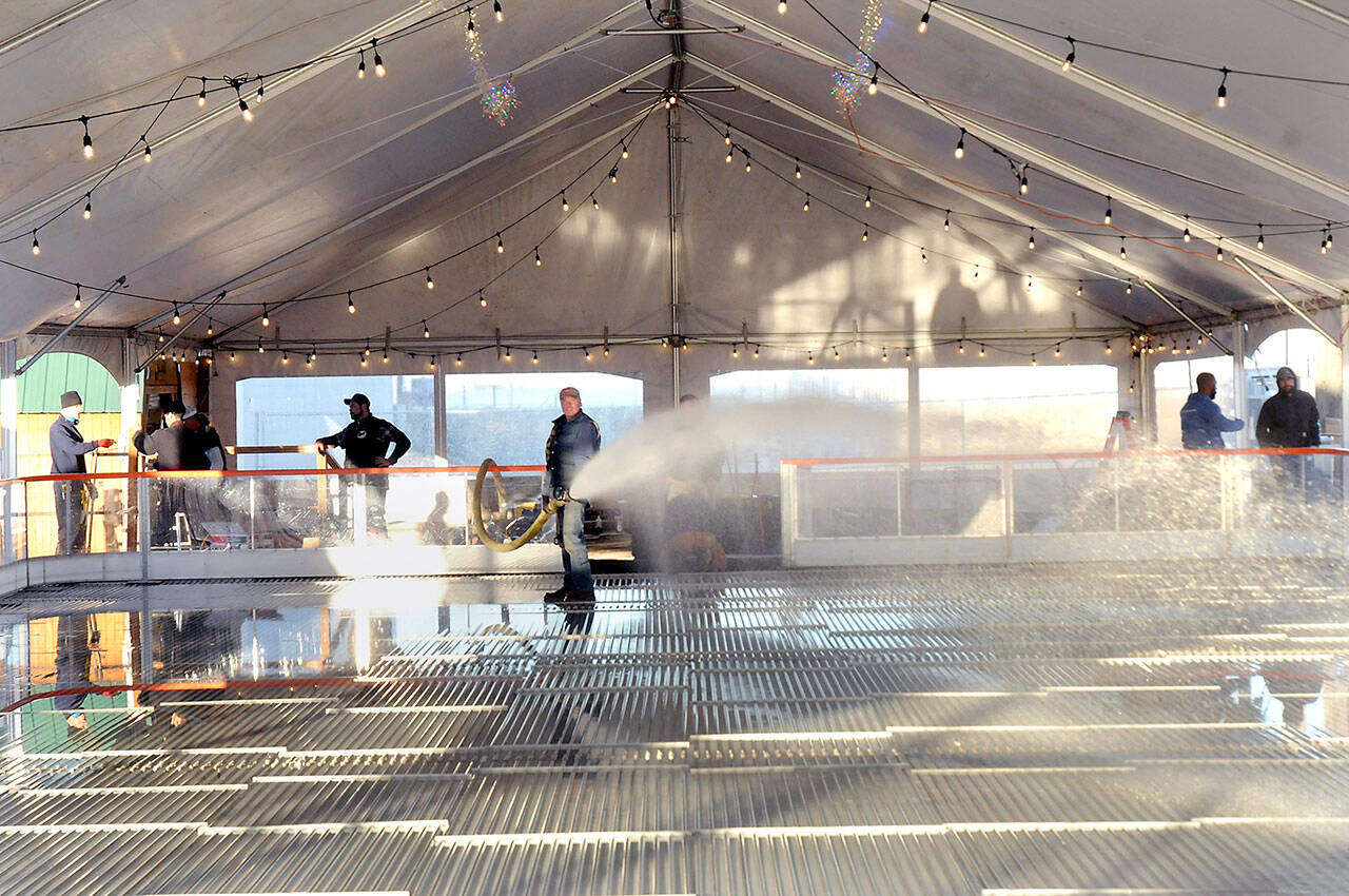 Tommy Robertson of Port Angeles, center, sprays water onto chiller coils that will eventually create the ice skating surface at the Port Angeles Ice Village on Tuesday in downtown Port Angeles. (Keith Thorpe/Peninsula Daily News)