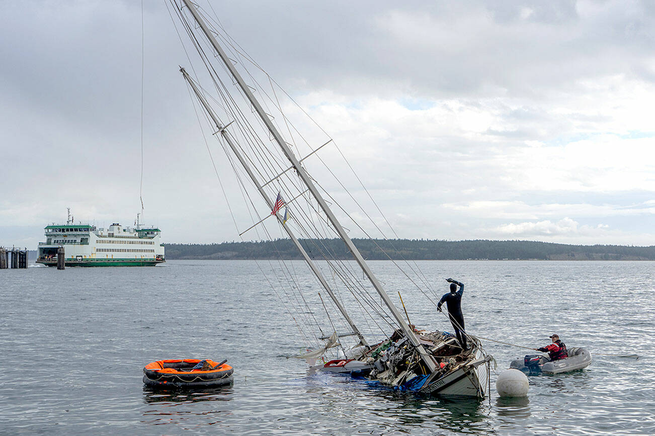 Unidentified men work to try to pull the partially sunken, 36-foot ketch Touchstone off the sand after it was blown off its anchorage during a windstorm that blew across Port Townsend Bay on Friday night and Saturday morning. Another round of gusty winds is expected today. (Steve Mullensky/for Peninsula Daily News)