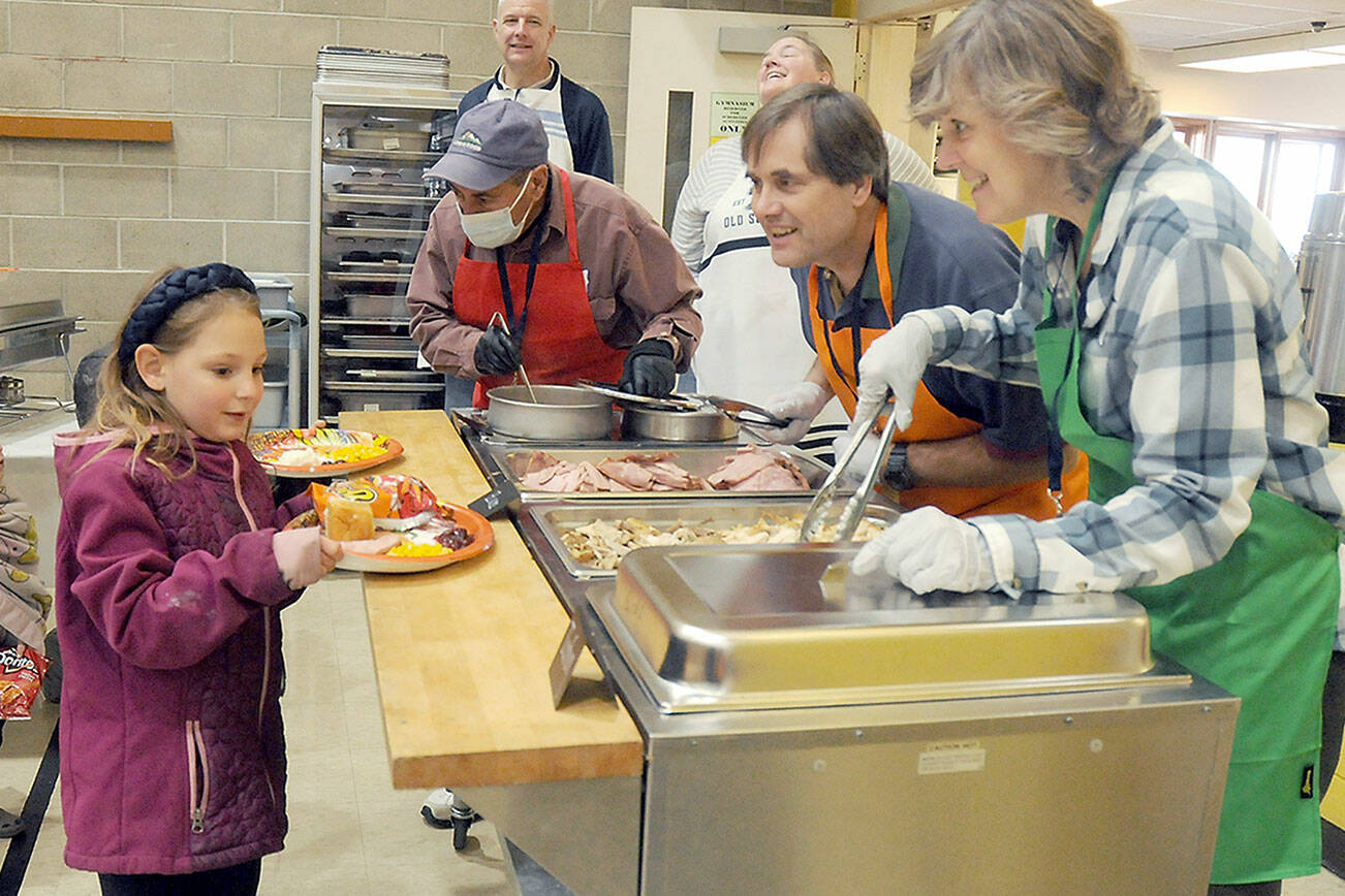 Anna-Marie Tax, 7, of Port Angeles and her brother A.J. Tax, 4, behind, are served by volunteers, from left, Phil Becillis, Lorenz Sololmann and Patty Sollman during Thursday’s Community Dinner at Queen of Angeles community hall in Port Angeles. Hundreds of people took part in the free meal, which featured traditional Thanksgiving fare, dessert and the companionship of other community members. (Keith Thorpe/Peninsula Daily News)