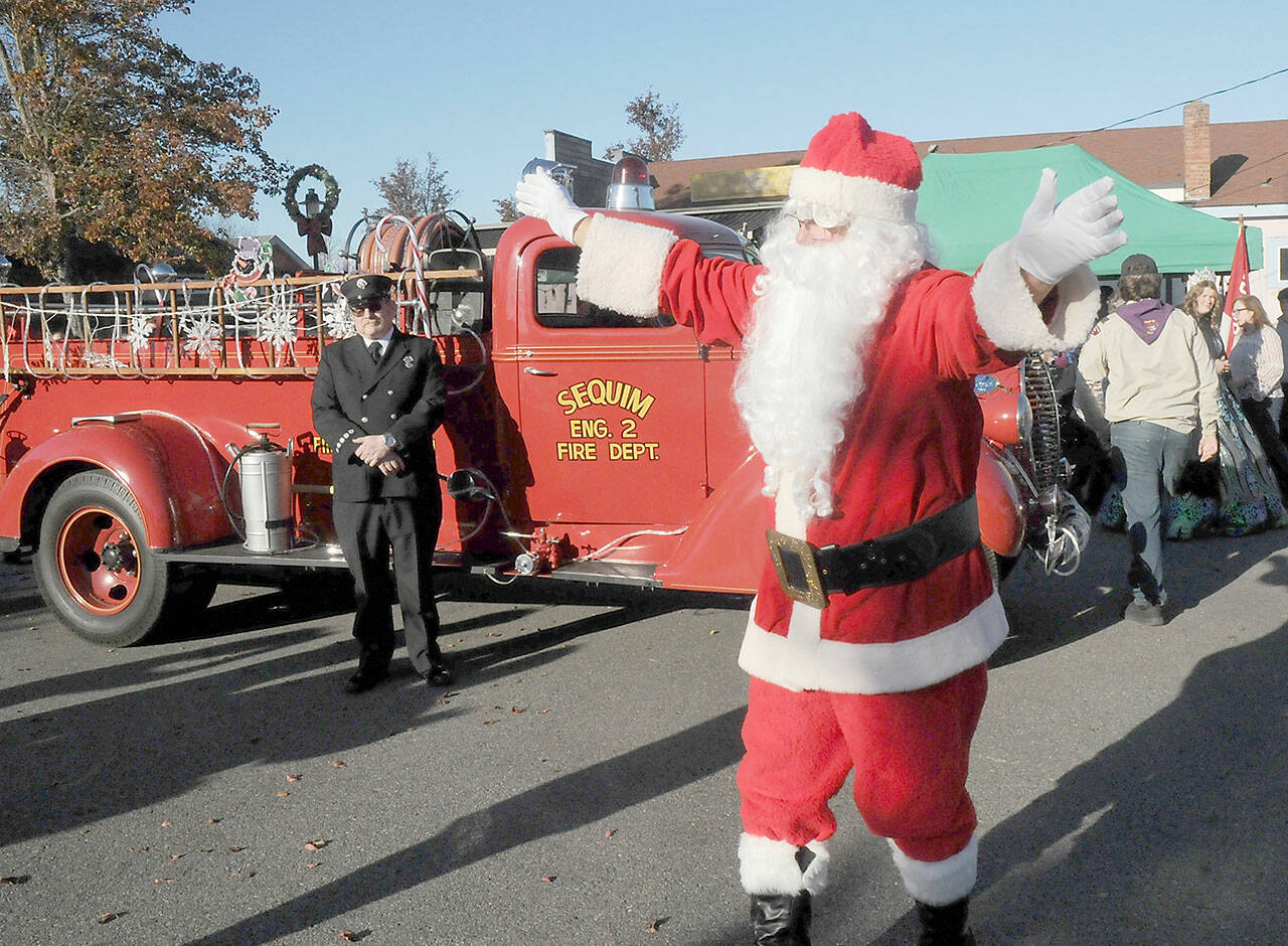 Santa Claus, portrayed by Stephen Rosales of Sequim, waves to the crowd after his arrival by vintage fire truck at Centennial Place in downtown Sequim on Saturday, part of the city’s Hometown Holidays celebration. Santa, accompanied by Irrigation Festival royalty, greeted children next to the city’s Christmas tree in an event that also featured music by the Sequim City Band and a lighted tractor parade. (Keith Thorpe/Peninsula Daily News)