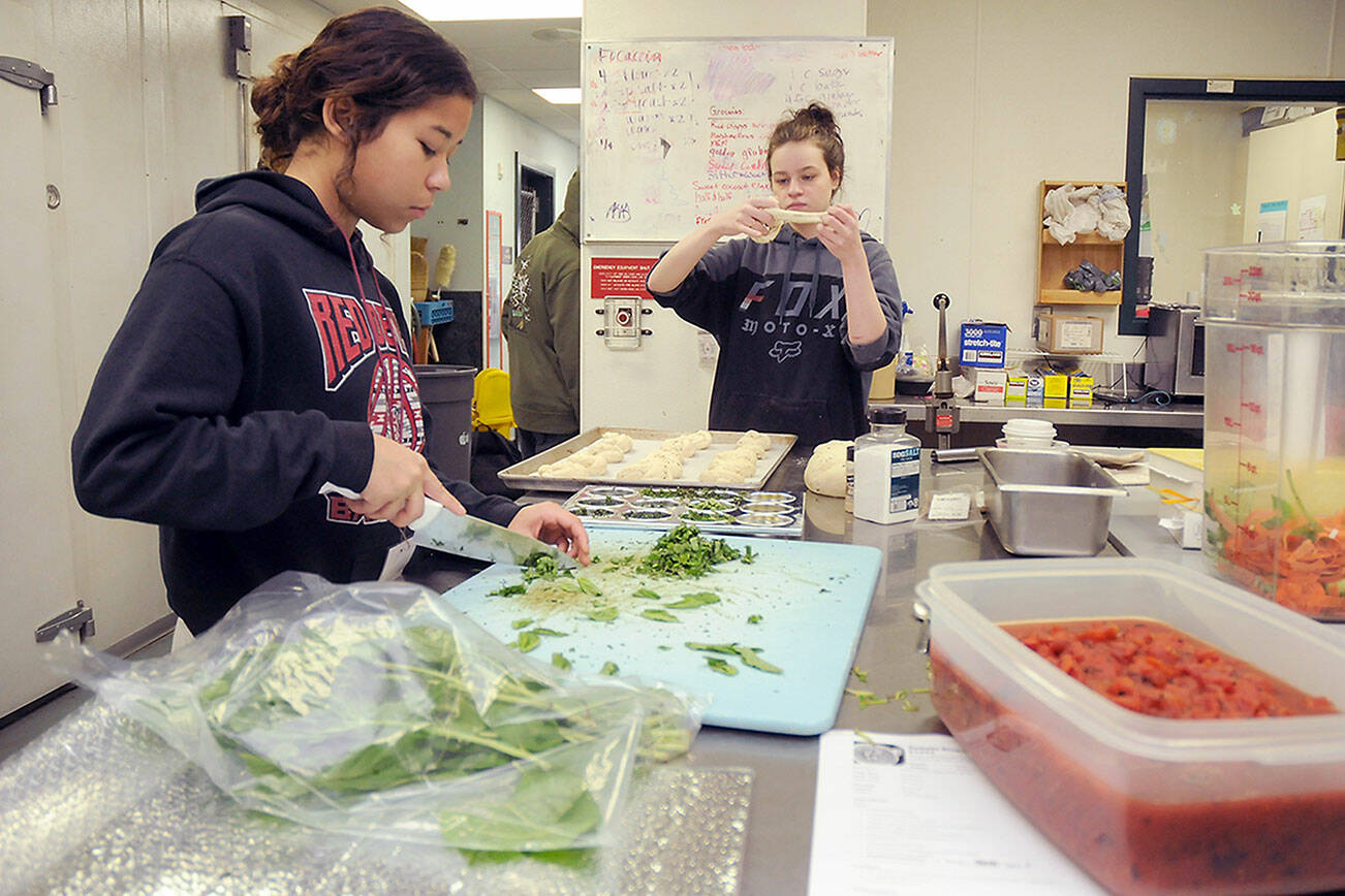 KEITH THORPE/PENINSULA DAILY NEWS
Salish Sea Ecotourism and Hospitality students Julia Livingston, 17, left, dices basil while Trinity Williams, 18, creates garlic bread twists at the Port Angeles School District's commercial kitchen classroom.