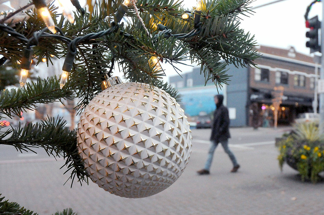 A Christmas ornament hangs from the downtown Port Angeles Christmas tree as a pedestrian walks past the plaza at the Conrad Dyar Memorial Fountain. The tree, towering above the intersection at First and Laurel streets, will remain illuminated through the holiday season. (Keith Thorpe/Peninsula Daily News)