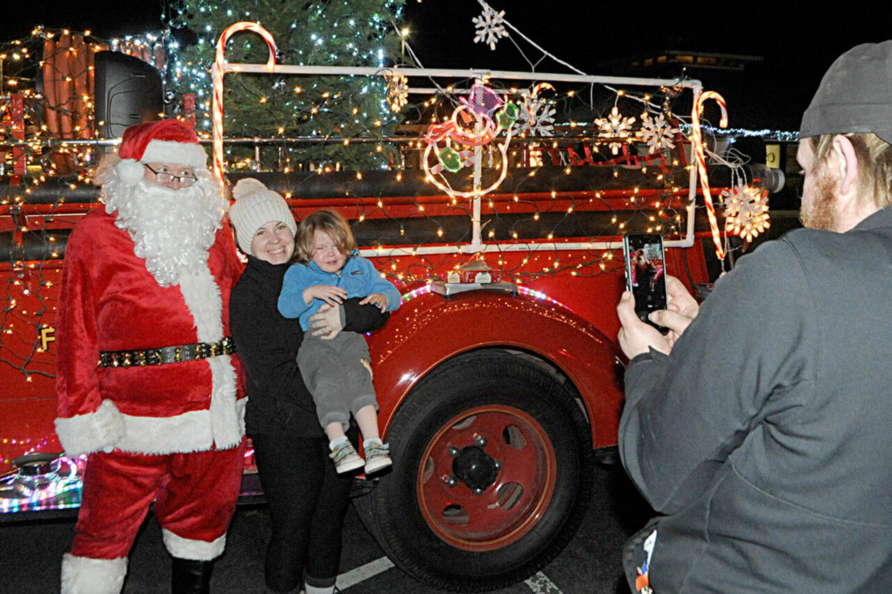 Veronica Weatherly holds her son Tucker for a photo-op with Santa Claus in 2021 as her husband Doug takes a photo. Santa’s Toy and Food Fire Brigade tours Sequim again Dec. 4-7. (Matthew Nash/Olympic Peninsula News Group)