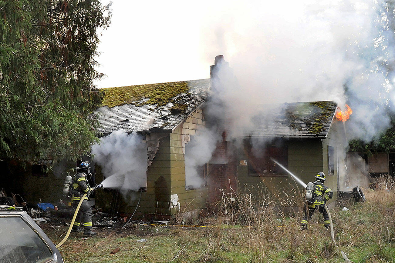Port Angeles firefighter Ryan Gosling, left, and Samantha Harik work to extinguish a blaze at an unoccupied house at 1338 W. Lauridsen Blvd. on the edge of Port Angeles on Saturday. (Keith Thorpe/Peninsula Daily News)