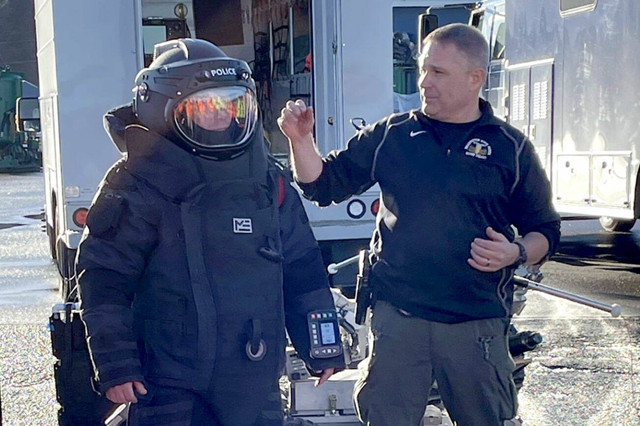 Washington State Patrol Bomb Squad commander Cliff Pratt, right, describes and explains the function of a blast suit worn by bomb technician Dan Betts to security staff at the Port of Port Angeles. The squad visited the port Friday for a presentation on its response protocols, tools and equipment. (Paula Hunt/Peninsula Daily News)