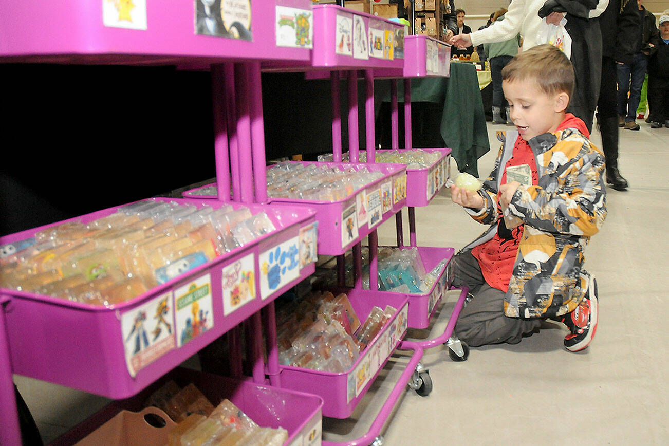 Enzo Ramirez, 4, of Port Angeles clutches his dollar bill while searching for an affordable gift to purchase at a vendor table set up by Port Angeles-based Power Up Perler & Soaps during Saturday’s Holiday Market at Vern Burton Community Center in Port Angeles. The market featured dozens of gift and craft tables by local artisans, including a donation and craft table benefiting Peninsula Friends of Animals. (Keith Thorpe/Peninsula Daily News)