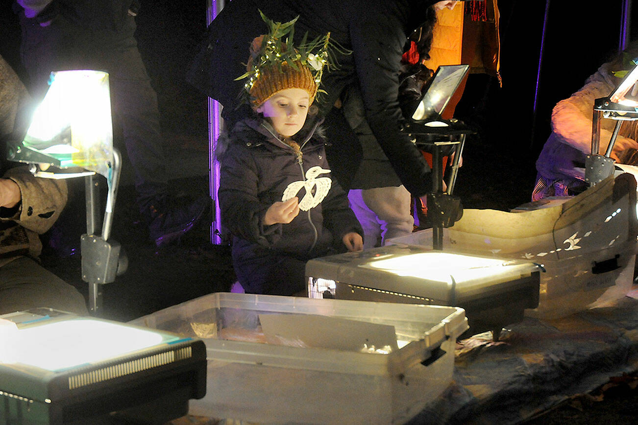 Farrah Friswold, 5, of Port Angeles looks at a silhouette of a bird for placement on an overhead projector at an interactive light station at Wintertide on Saturday in Webster’s Woods Sculpture Park at the Port Angeles Fine Arts Center. The Wintertide Festival of Lights featured a variety of hands-on activities, food, music, a fire dancing exhibition, a lantern walk and a seasonal selection of illuminated sculptures, as well as an ongoing Makers Market of artistic gifts in the fine art center gallery. (Keith Thorpe/Peninsula Daily News)