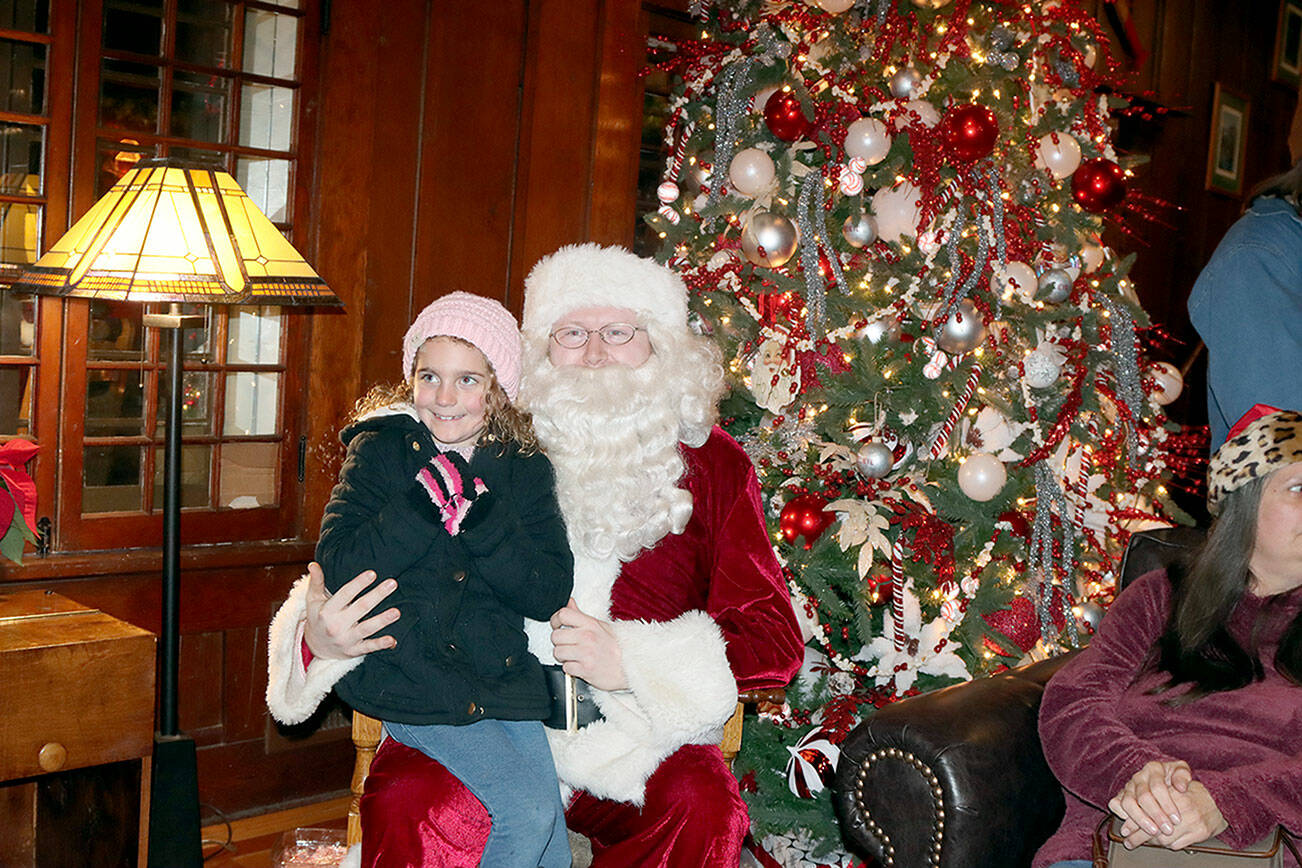 Kinsley Clemens, 6, of Port Angeles sits on Santa’s lap while family members take photos of the event. Santa got to visit many children who went to the Lake Crescent Lodge to enjoy the holiday spirit. (Dave Logan/for Peninsula Daily News)