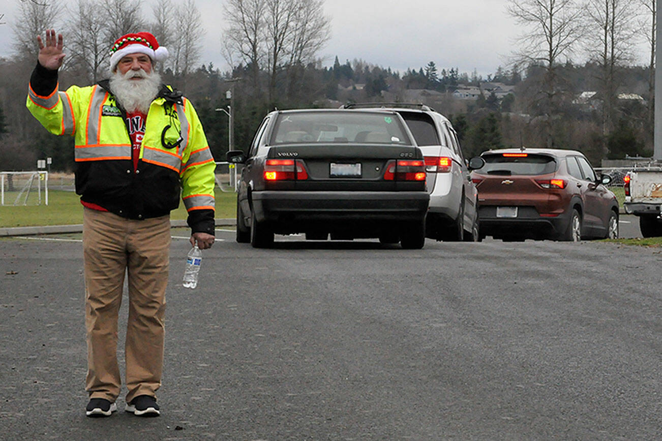 Butch Zaharias, a captain and division chief with the Community Emergency Response Team (CERT), checks in on drivers and fellow CERT members in festive garb during the Family Holiday Meal Bag distribution in Sequim’s Carrie Blake Park. (Matthew Nash/Olympic Peninsula News Group)