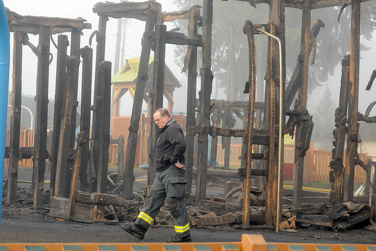 Assistant Fire Chief Mike Sanders walks past the burnt remains of a play structure at the Dream Playground on Wednesday morning. (Keith Thorpe/Peninsula Daily News)
