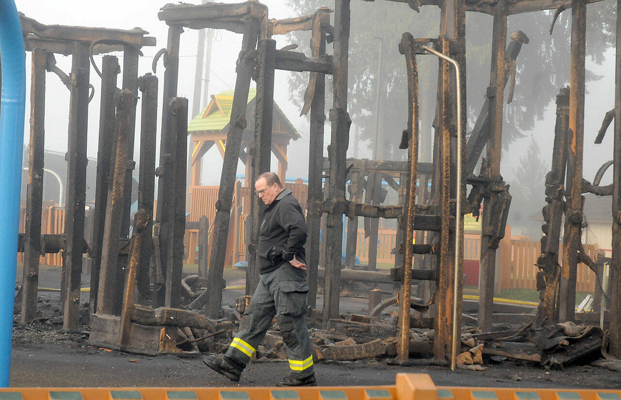 Assistant Fire Chief Mike Sanders walks past the burnt remains of a play structure at the Dream Playground on Wednesday morning. (Keith Thorpe/Peninsula Daily News)