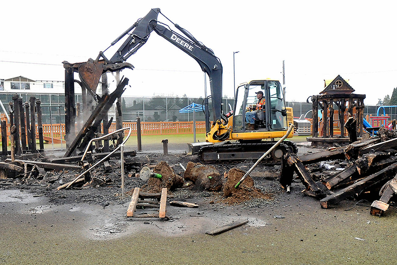 An excavator operated by Jad Groves of the Port Angeles Public Works Department removes the charred remains of the treehouse structure at the Dream Playground at Erickson Playfield on Thursday after much of the playground was destroyed by fire early Wednesday morning. (Keith Thorpe/Peninsula Daily News)