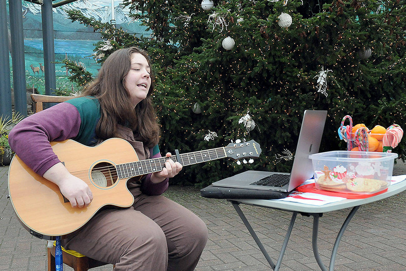 KEITH THORPE/PENINSULA DAILY NEWS
Kenzie Carney of Port Angeles plays guitar and sings while giving away candy canes, oranges and homemade cookies in front of the downtown Port Angeles Christmas tree at the Conrad Dyar Memorial Fountain on Tuesday. Carney said the effort was an opportunity to spread holiday cheer to those who might need it on the day after Christmas.