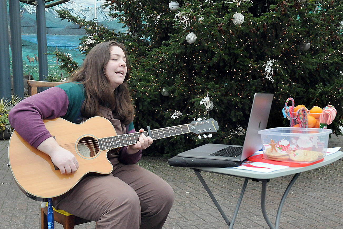 Kenzie Carney of Port Angeles plays guitar and sings while giving away candy canes, oranges and homemade cookies in front of the downtown Port Angeles Christmas tree at the Conrad Dyar Memorial Fountain on Tuesday. (KEITH THORPE/PENINSULA DAILY NEWS)