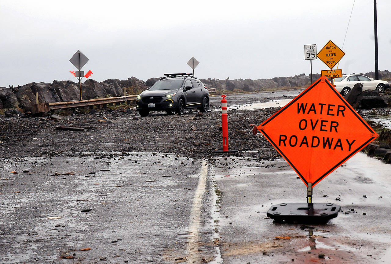 A car picks its way through a field of rocks and other debris pushed by wind-driven waves and high tides over Ediz Hook Road in Port Angeles on Tuesday. The city Public Works Department has closed the road. (Keith Thorpe/Peninsula Daily News)