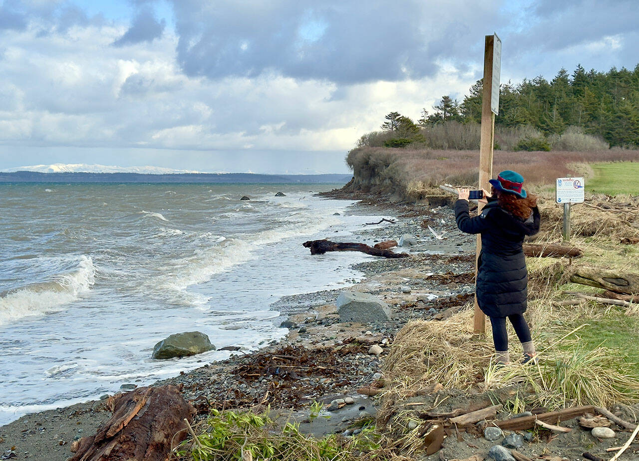 Port Townsend’s Margo Karler uses her cell phone to photograph wave action at North Beach in Port Townsend on Thursday. (Steve Mullensky/for Peninsula Daily News)