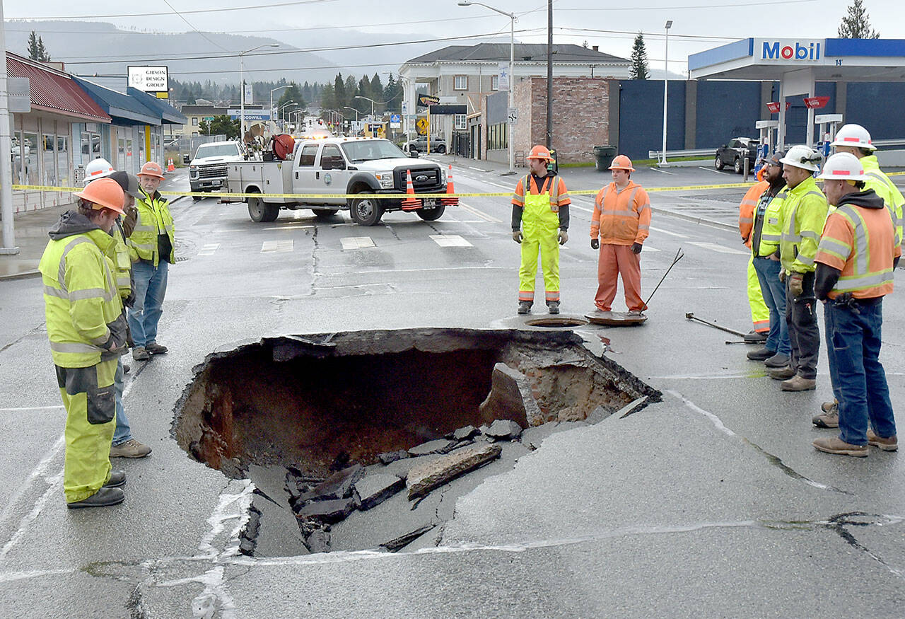 Port Angeles Public Works and Washington State Department of Transportation officials examine a sinkhole in the middle of Fifth and Lincoln streets in Port Angeles on Wednesday after water from a broken water main tore up the pavement. (Keith Thorpe/Peninsula Daily News)