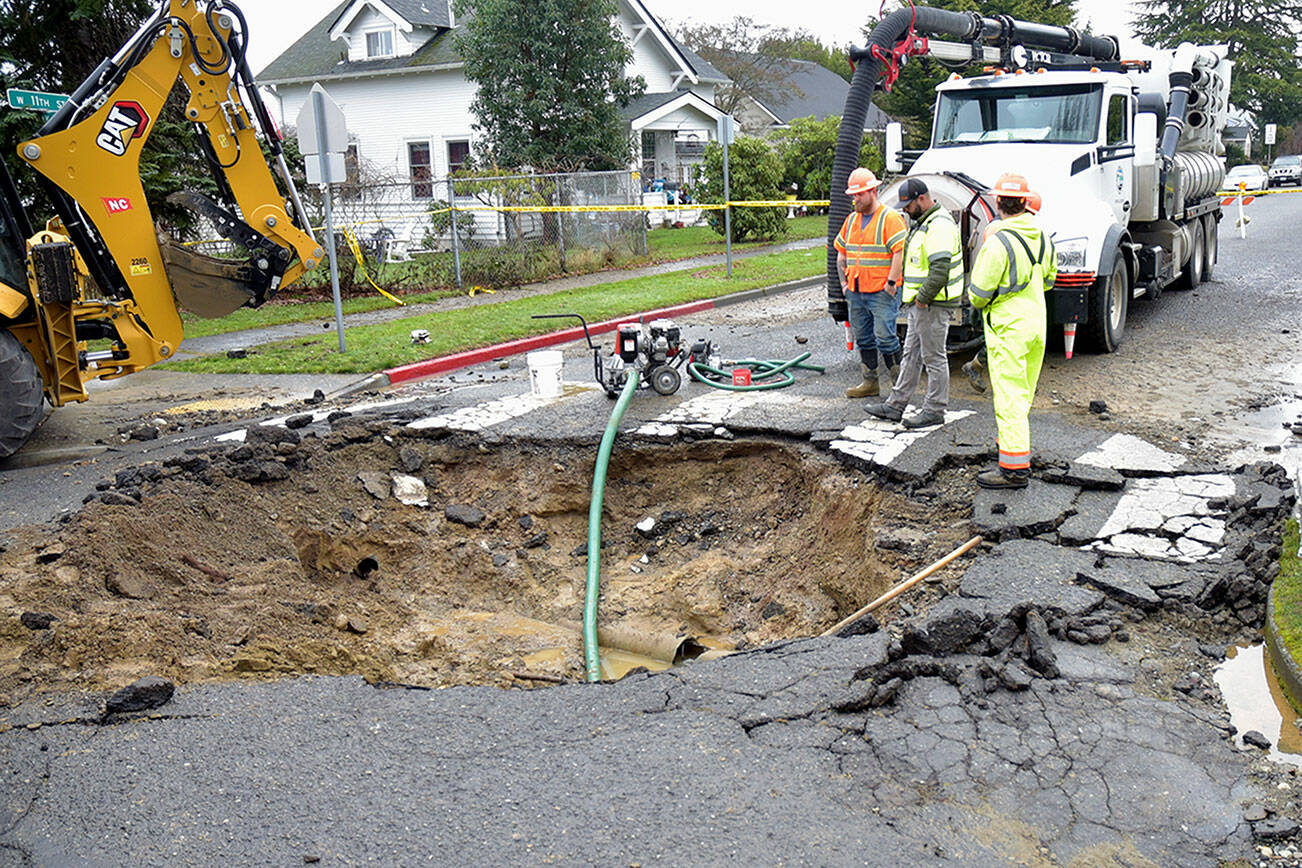 A Port Angeles Public Works crew examines the hole left at 11th and Oak streets after a water main break sent a geyser of water into the air Saturday morning, damaging the road surface. (Keith Thorpe/Peninsula Daily News)