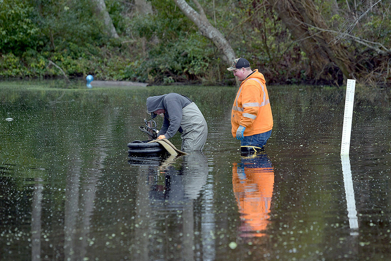 Michael Poats, left, and Brody Merritt of the Port Angeles stormwater department work to install a pump to remove standing water from a flooded area near the playground at Shane Park in Port Angeles on Wednesday. The pool of standing water, which is up to 3 feet deep in places and has at times covered the nearby play equipment, is to be pumped to a nearby storm drain. (Keith Thorpe/Peninsula Daily News)