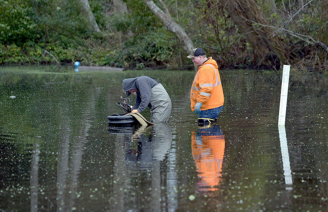 Michael Poats, left, and Brody Merritt of the Port Angeles stormwater department work to install a pump to remove standing water from a flooded area near the playground at Shane Park in Port Angeles on Wednesday. The pool of standing water, which is up to 3 feet deep in places and has at times covered the nearby play equipment, is to be pumped to a nearby storm drain. (Keith Thorpe/Peninsula Daily News)