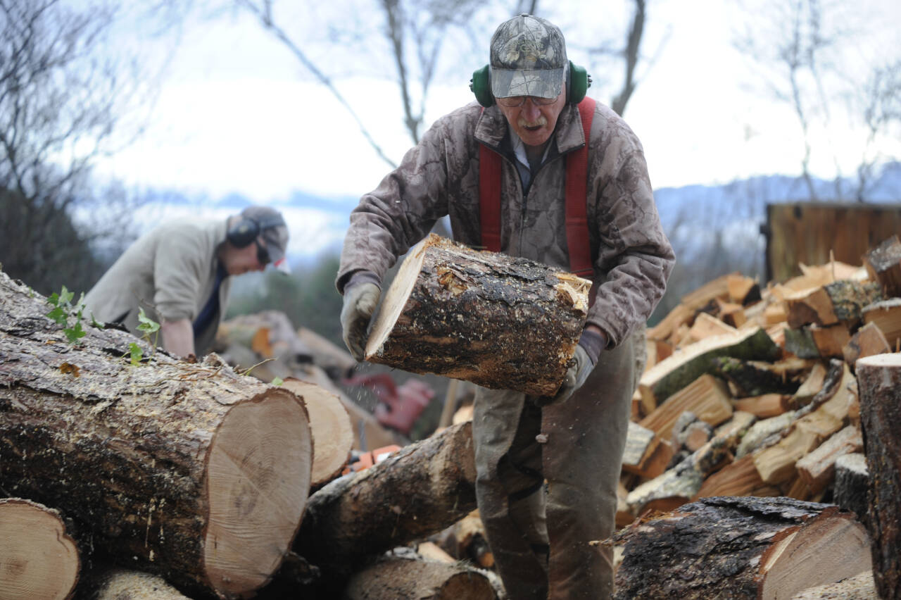 Wally Jenkins tosses a piece of wood into a pile as he and fellow woodcutters compile cords of firewood to sell, using the funds for the Path From Poverty nonprofit. (Michael Dashiell/Olympic Peninsula News Group)