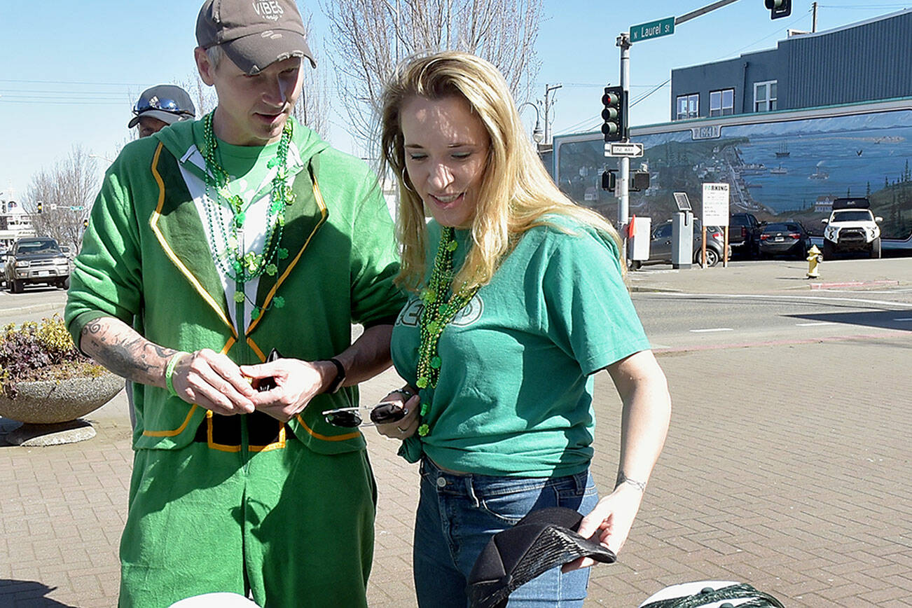 Casey and Karen Proud, both of Sequim, look at a selection of St. Patrick’s Day hats and other souvenirs for participating in Saturday’s Shamrock Shuffle & Pub Crawl in downtown Port Angeles. The event, a benefit for the Hurricane Ridge Winter Sports Education Foundation, allowed crawlers to receive six tasting tokens for libations at participating bars and restaurants in the downtown area with a drawing for additional prizes. Numerous downtown businesses also offered sale discounts for purchases during the crawl. (Keith Thorpe/Peninsula Daily News)