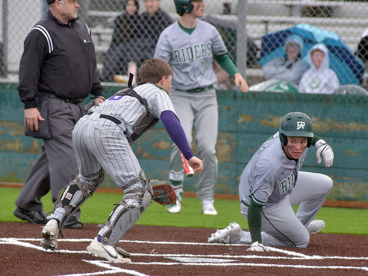 KEITH THORPE/PENINSULA DAILY NEWS Port Angeles’ Kaleb Mullen, right, looks back at North Kitsap catcher Greyson Prichard after making it home in the second inning as Mullen’s teammate, Rylan Politika waits to bat on Tuesday at Volunteer Field.