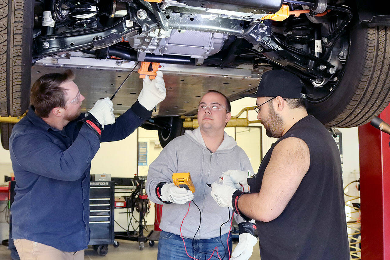 Instructor Josh Taylor, left, points out the workings of an electric vehicle on Wednesday at the Auto Technology Certification Program at Peninsula College. Nick Schommer, center, and Brian Selk get ready to do some testing on the electric auto’s parts from underneath the vehicle. (Dave Logan/for Peninsula Daily News)