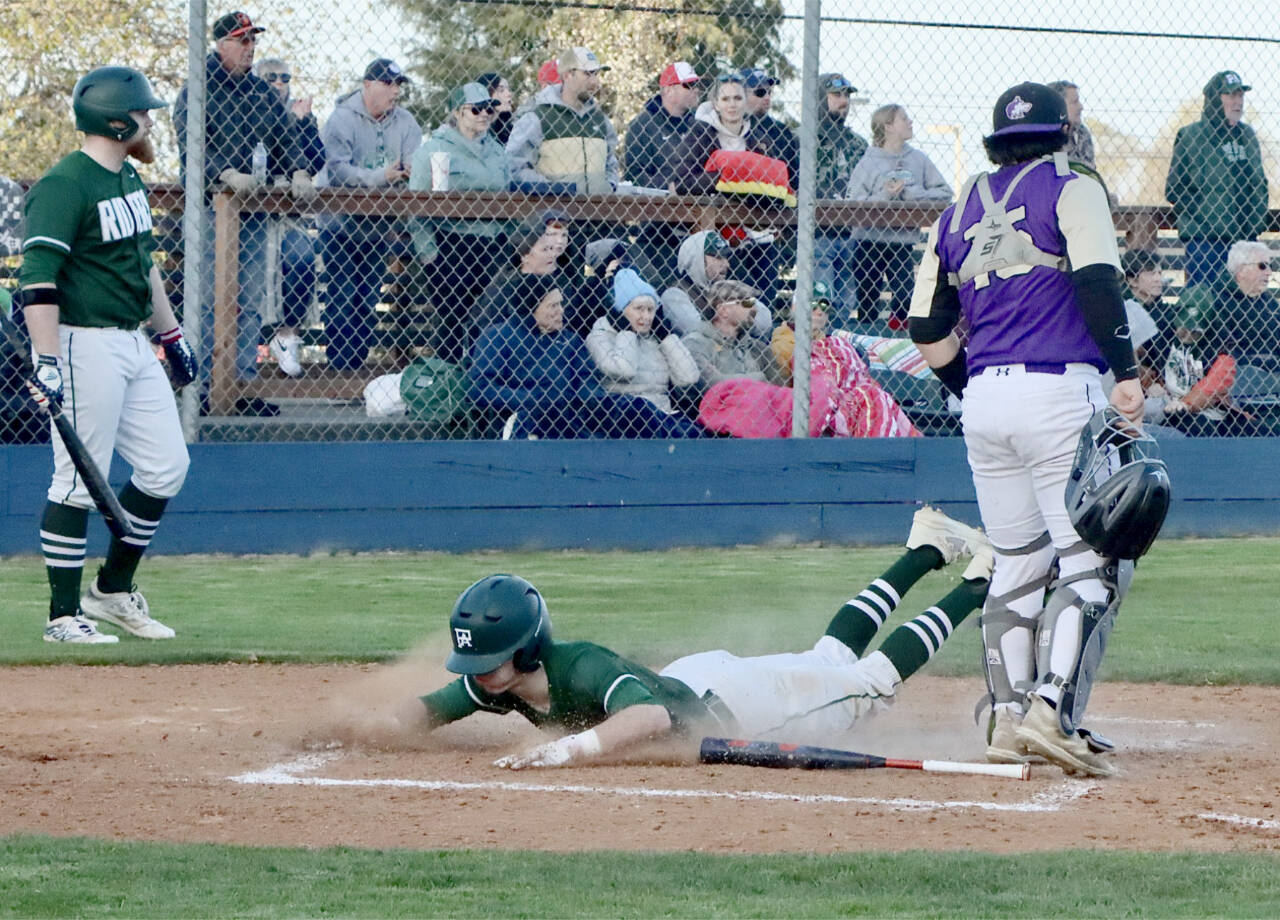 Port Angeles' Alex Angevine slides home safely against Sequim as catcher Ayden Holland waits for a throw. In the on-deck circle is Port Angeles' Ezra Townsend. (Dave Logan/for Peninsula Daily News)