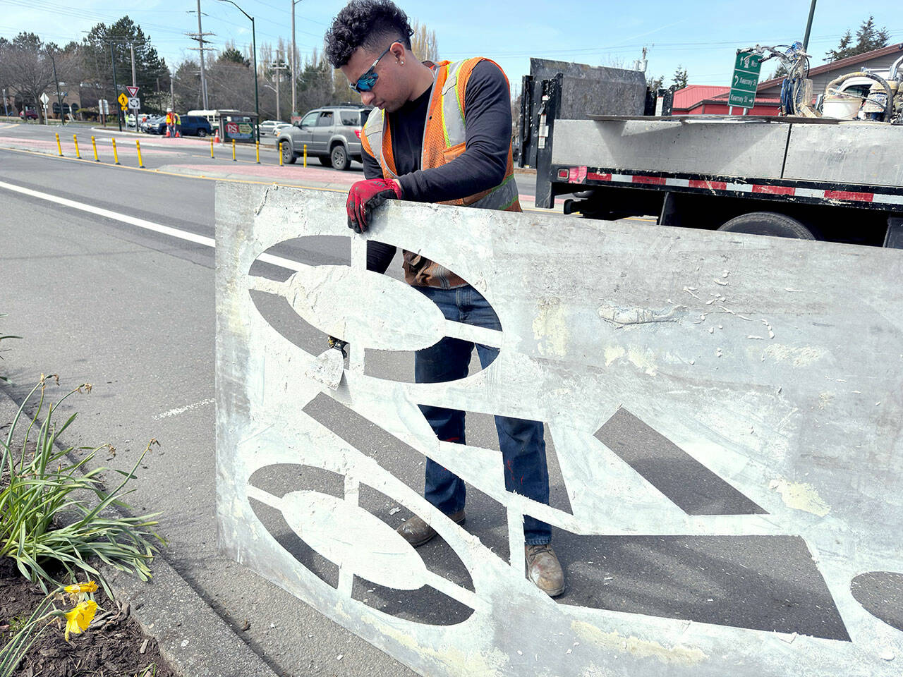 Fernando Cruz of Auburn, an employee of Specialized Pavement Marking in Pacific, cleans off a sign he used to paint a bicycle lane on Sims Way and Kearney Street, the site of the new roundabout. The workers needed at least two days of 47 degrees or above in order to paint the pedestrian crosswalks and other necessary markings. (Steve Mullensky/for Peninsula Daily News)
