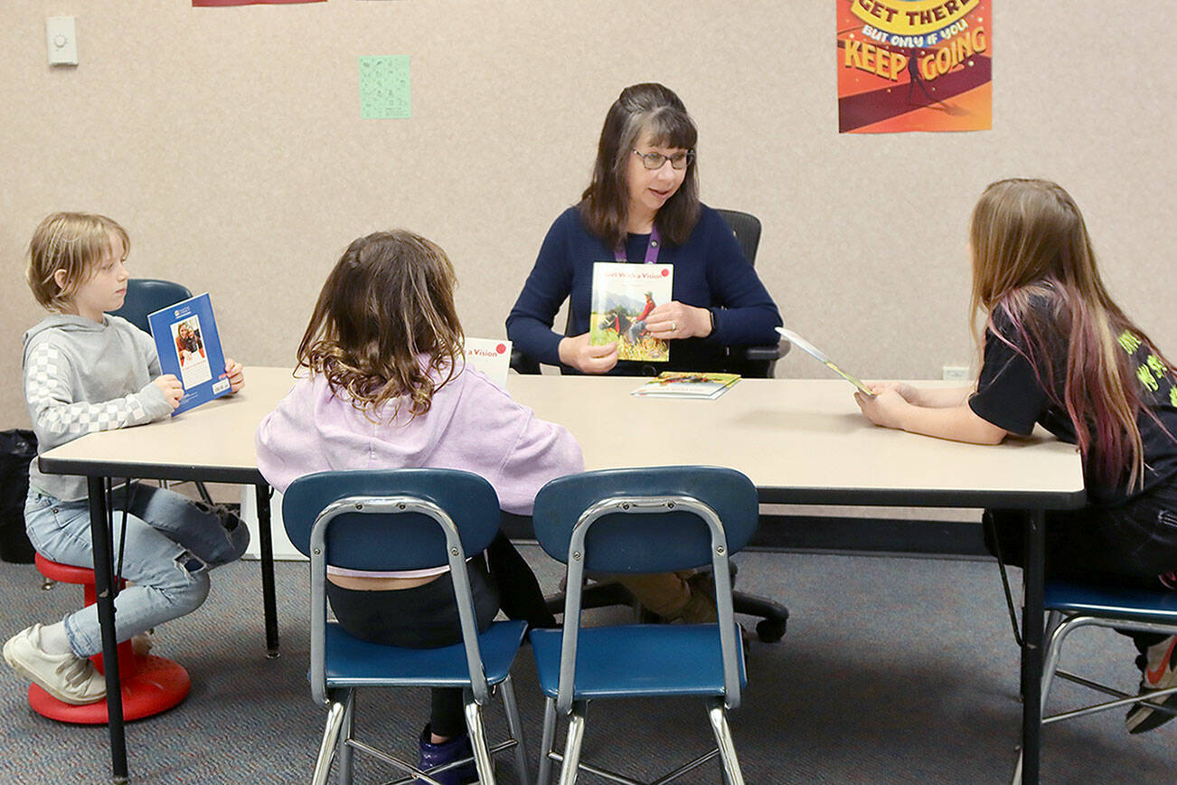 Becca Paul, a paraeducator at Jefferson Elementary in Port Angeles, helps introduce a new book for third-graders, from left, Margret Trowbridge, Taezia Hanan and Skylyn King, to practice reading in the Literacy Lab. The book is entitled “The Girl With A Vision.” (Dave Logan/for Peninsula Daily News)
