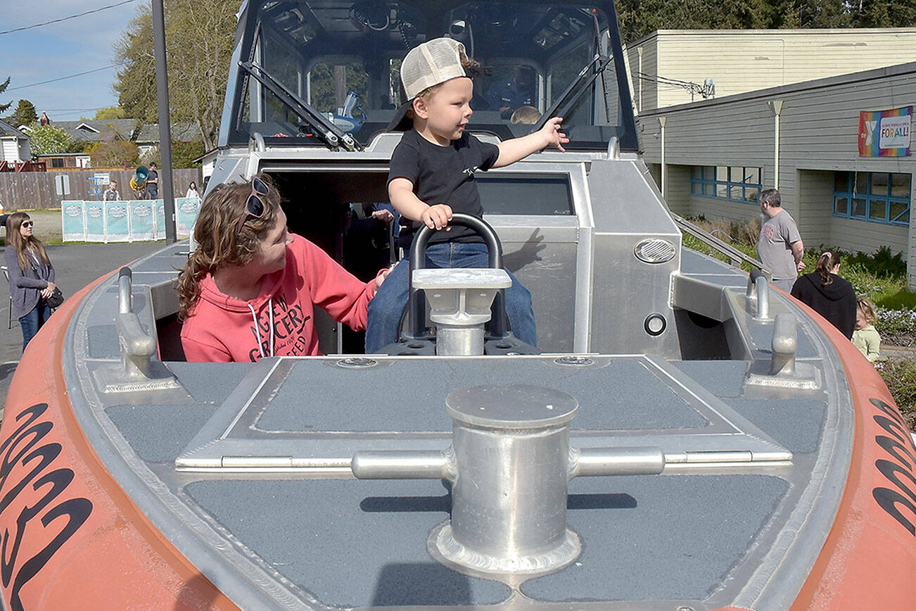 Clayton Hergert, 2, along with is mother, Mandy Hergert of Port Angeles, sit at the bow of a U.S. Coast Guard response boat on display during Saturday’s Healthy Kids Day at the Port Angeles YMCA. The event, hosted by all three Olympic Peninsula YMCA branches, featured children’s activities designed to promote a healthy lifestyle and a love for physical activity. (Keith Thorpe/Peninsula Daily News)