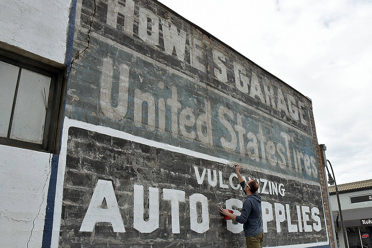 Kyle Zimmerman, co-owner of The Hub at Front and Lincoln streets in downtown Port Angeles, adds a new coat of paint on Wednesday to an advertising sign on the back of his building that was uncovered during the demolition of a derelict building that once hid the sign from view. Zimmerman said The Hub, formerly Mathews Glass and Howe's Garage before that, is being converted to an artist's workspace and entertainment venue with an opening set for late May or early June. Although The Hub will have no control over any new construction that might later hide the automotive signs, Zimmerman said restoring the paint is an interesting addition to the downtown area for as long as it lasts. (Keith Thorpe/Peninsula Daily News)