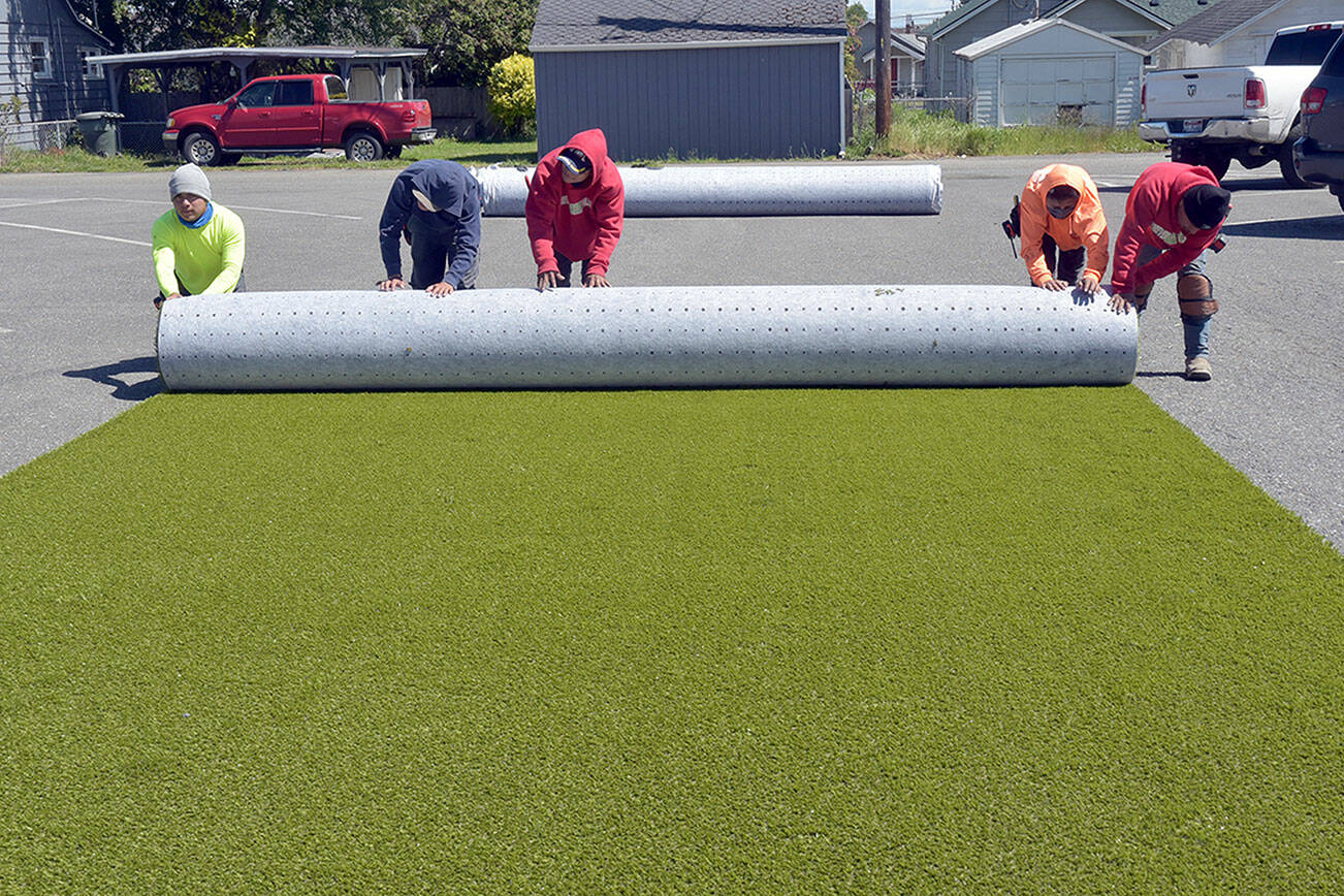 A work crew from the Texas-based ForeverLawn rolls up a piece of cut playground surface in the parking lot of Erickson Playfield in preparation for installation at the nearby Dream Playground in Port Angeles. The crew was contracted to install the padded play area after a five-day community build last week to replace portions of the playground that were destroyed by arson in December. (Keith Thorpe/Peninsula Daily News)