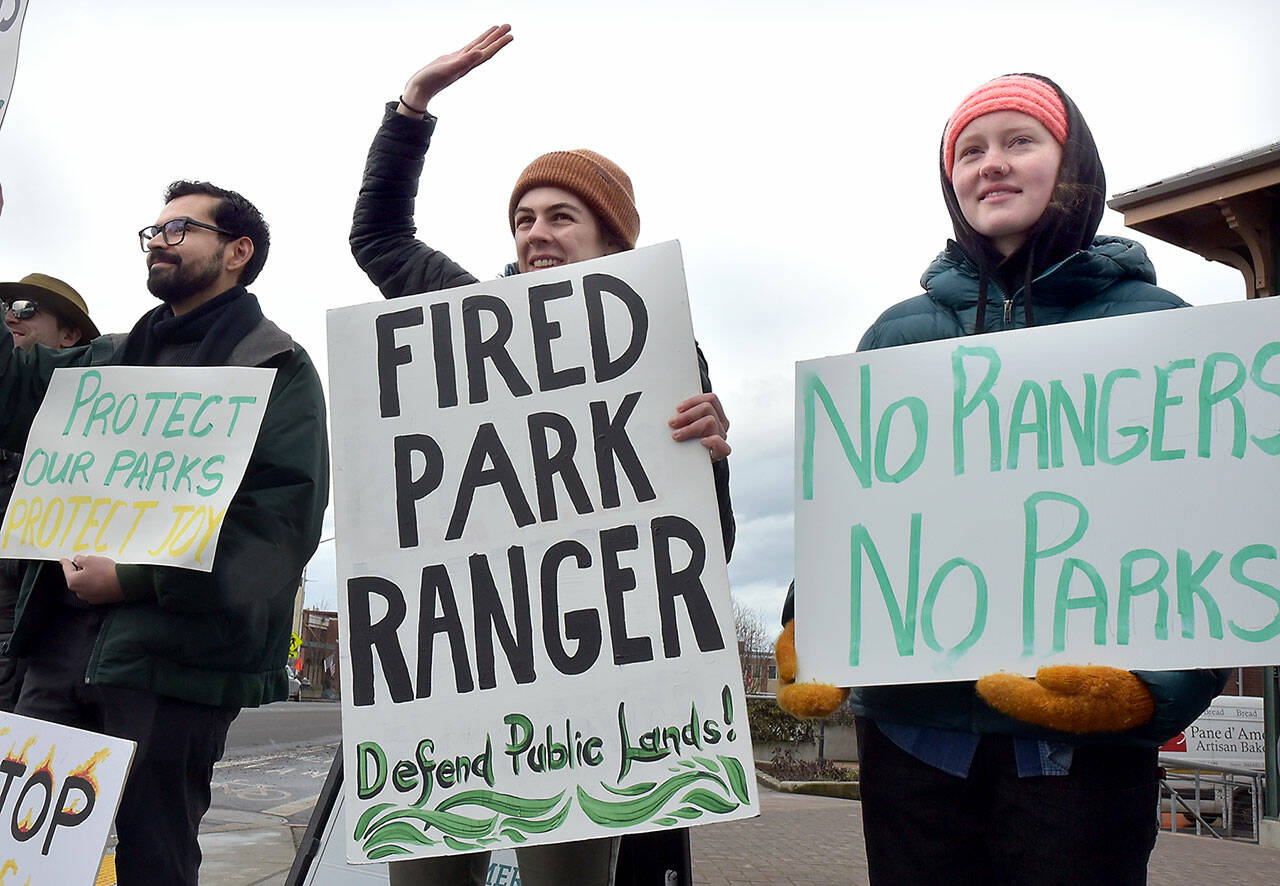 Hazel Galloway, a recently laid-off science communications specialist with the National Park Service, center, is flanked by Andy Marquez, a marine science student assisting Olympic National Park, left, and Mari Johnson, a supervisor with ONP partner Washington Conservation Corps during a protest at The Gateway in Port Angeles against the Trump administrations downsizing of the NPS workforce. (Keith Thorpe/Peninsula Daily News)