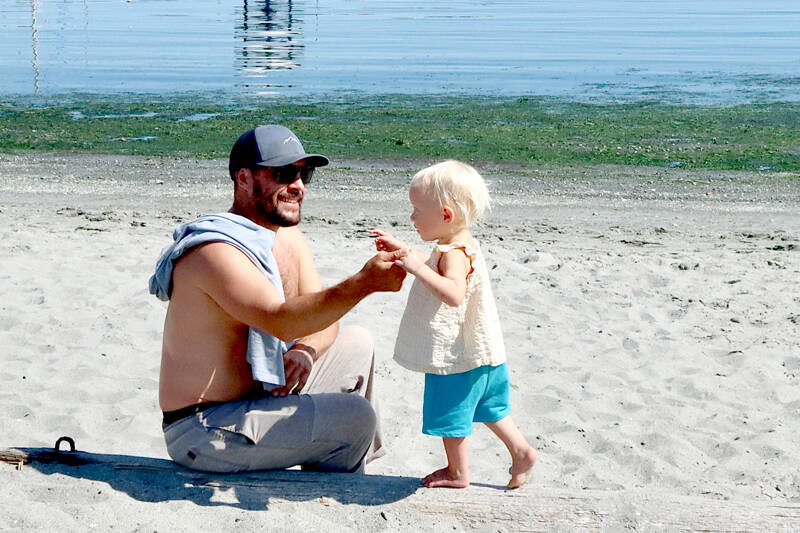 Matthew Hara of Port Angeles helps Ayla Gillies, 2, balance on a log on the sandy shores of Hollywood Beach in downtown Port Angeles. Summer temperatures are forecast to be in the mid-70s for the rest of the week on the North Olympic Peninsula. (Dave Logan/for Peninsula Daily News)