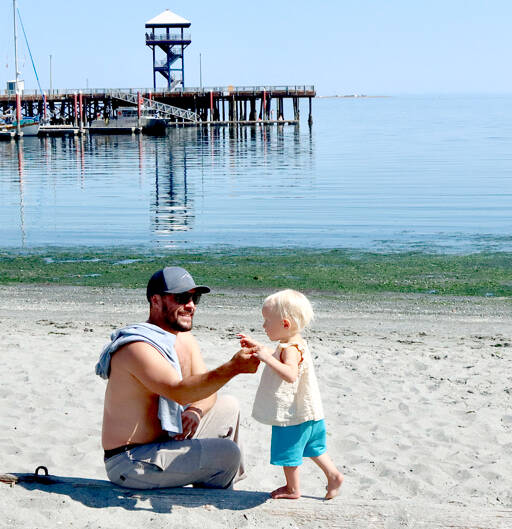 Matthew Hara of Port Angeles helps Ayla Gillies, 2, balance on a log on the sandy shores of Hollywood Beach in downtown Port Angeles. Summer temperatures are forecast to be in the mid-70s for the rest of the week on the North Olympic Peninsula. (Dave Logan/for Peninsula Daily News)