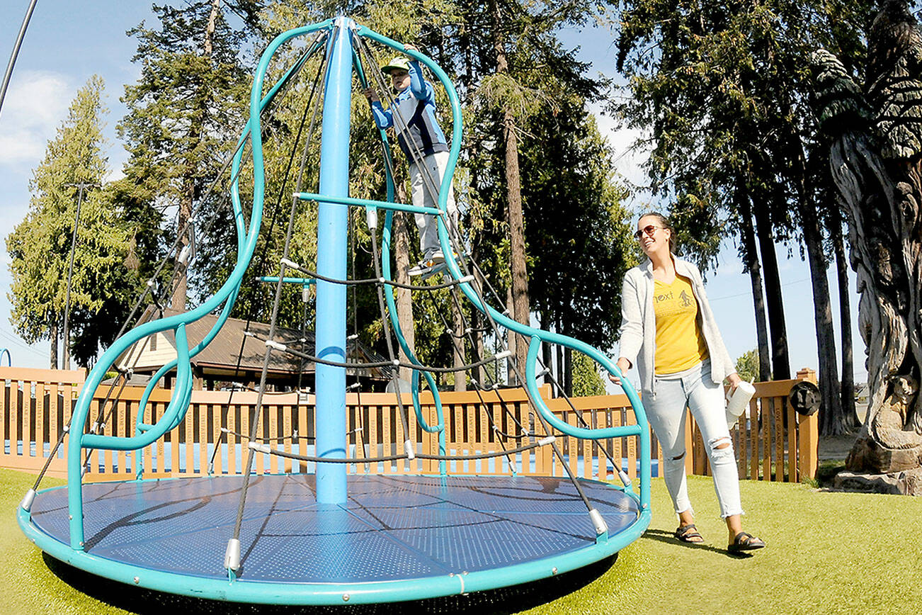 Carlyn Beebe of Forks pushes a merry-go-round toy as her son, Lane, 6, takes a ride on Tuesday at the Dream Playground at Erickson Playfield in Port Angeles. The pair took time out from errands for a visit to the popular park. (Keith Thorpe/Peninsula Daily News)
