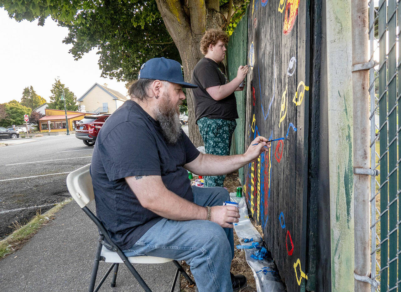 Jesse Adams, front, of Port Townsend, and son Evan of Allyn paint eyes on a section of the fence surrounding Port Townsends Memorial Field as their contribution to the Outsiders Street Art Project Port Townsend during Jefferson Countys first community public art project. Adams project, titled Eye Strain, had to be submitted for approval before work could begin. Each artist had an 8-foot section of fence to work on. The fence will be taken down, most likely next spring, to be replaced with a new one. (Steve Mullensky/for Peninsula Daily News)