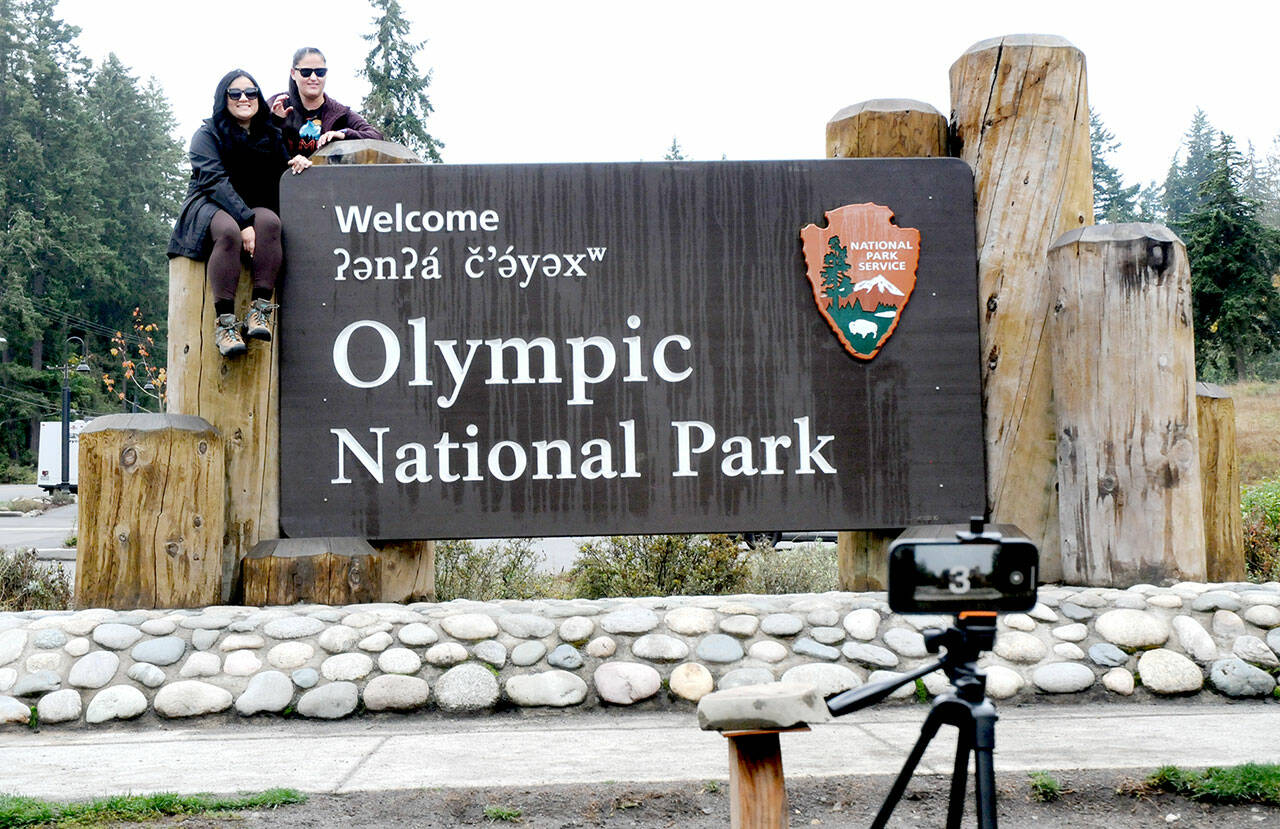 Lorena Miramontes Morley, left, and her spouse, Mandy Miramontes Morley, both of Anaheim, Calif., use a remote-controlled camera to take a self-portrait on the Olympic National Park entrance sign on Tuesday in Port Angeles. (Keith Thorpe/Peninsula Daily News)