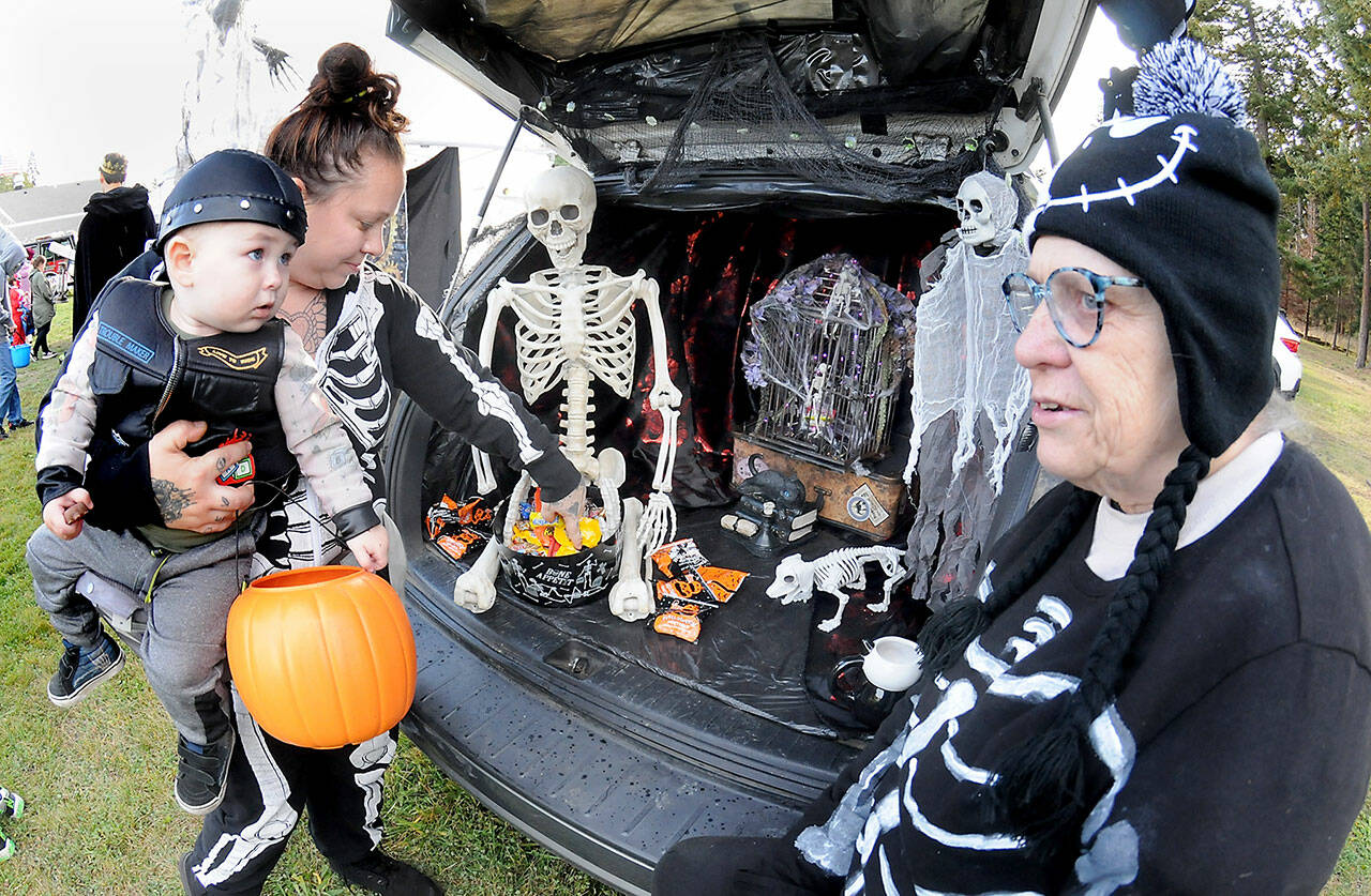 Jessica Topham of Sequim collects sweet treats for her son, Ivar Baker, 19 months, as Becky Rice looks on from her spookily decorated vehicle during Saturdays Country Fair and Trunk or Treat at the Sequim Prairie Grange north of Carlsborg. The Halloween-themed event featured food, games, pumpkin carving and scary treats, hosted by members of the grange. (Keith Thorpe/Peninsula Daily News)
