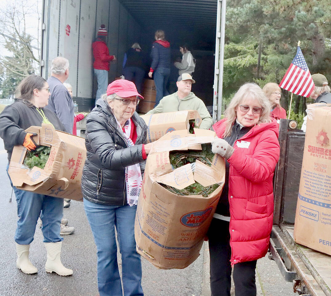 Donna Bower, left, and Kristine Konapaski, volunteers from the Michael Trebert Chapter of the Daughters of the American Revolution, unload one of the 115 boxes of Christmas wreaths and carry it to a waiting truck. (Dave Logan/For Peninsula Daily News)