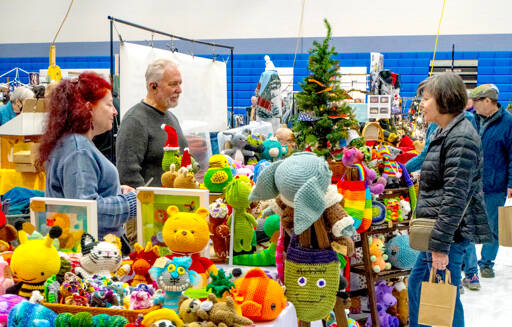 Pamela and Ernie Burnett, left, talk about their craft items, Amijurmi  Japanese small crocheted stuffed yarn creatures  to Tracey Harris of Marrowstone Island on Saturday during the first of two days at the 38th annual Chimacum Arts and Crafts Show at Chimacum High School. (Steve Mullensky/for Peninsula Daily News)