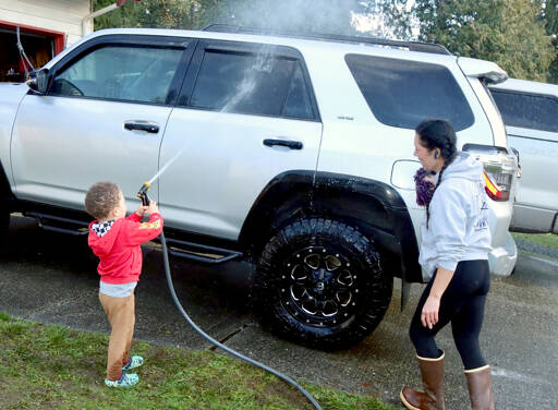 Logan Gear, 3 1/2, uses a garden hose to wash the family car in Port Angeles. His mother Rachel Gear said it was sunny and it was a chance to get out of the house and do something constructive. (Dave Logan/for Peninsula Daily News)