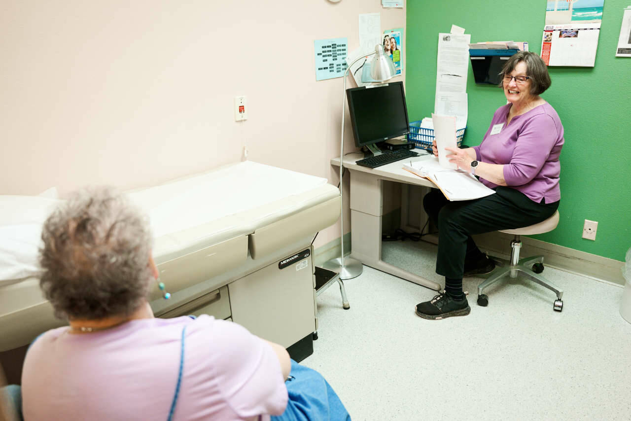 Kathi Gunn, right, a chronic healthcare nurse practitioner for the Dungeness Valley Health and Wellness Clinic, speaks with a patient. This year, thanks to volunteers and donors, the clinic will mark 25 years of providing free healthcare services to those who are uninsured or under-insured. (Austin James)