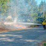 Clallam County Fire District No. 2 firefighters hose down the brush fire Tuesday. (Jay Cline/Clallam County Fire District No. 2)