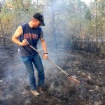 In the aftermath of a fire that started from a downed power line, JJ Anderson uses a rake to put out hot spots on the property of his brother PJ Anderson, located northeast of Spangle on Sunday. His brother&rsquo;s home was spared, but others were not so lucky. (Jesse Tinsley/The Spokesman-Review, via AP)