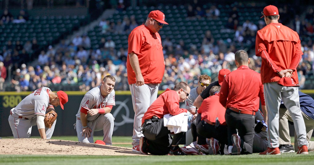 Los Angeles Angels infielders Andrelton Simmons, left, and Mike Trout kneel nearby as starting pitcher Matt Shoemaker is treated at right after being hit by a line drive from Seattle Mariners&rsquo; Kyle Seager in the second inning of a baseball game, Sunday, Sept. 4, 2016, in Seattle. (AP Photo/Elaine Thompson)