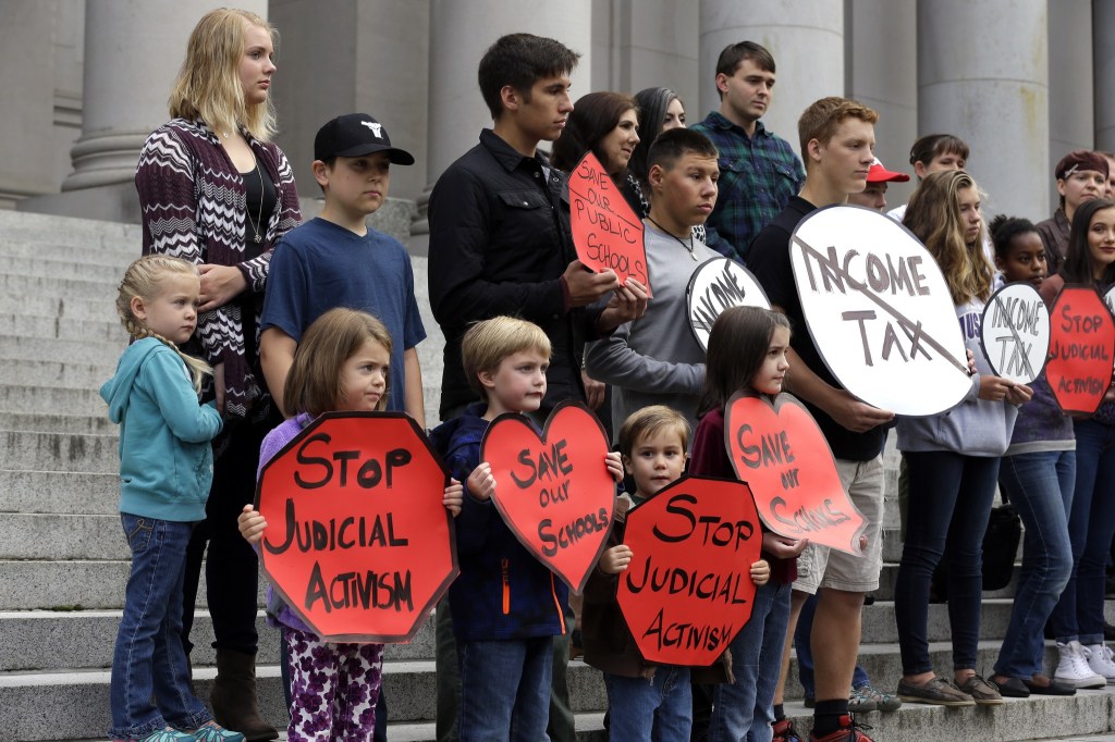 A group of people supporting public schools and opposed to further sanctions against the state regarding a lawsuit over education funding stands on the steps of the Temple of Justice in Olympia on Wednesday. (Ted S. Warren/The Associated Press)
